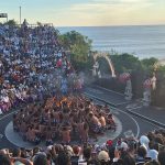 Sejarah Tari Kecak Bali: Pertemuan Timur dan Barat Sejarah Tari Kecak tidak bermula di panggung pertunjukan wisata, melainkan berakar jauh pada ritual keagamaan kuno yang disebut Sanghyang. Sanghyang merupakan tradisi tarian trance yang dilakukan untuk mengusir roh jahat, memohon perlindungan dari dewa, atau menyucikan komunitas dari wabah penyakit. Dalam ritual aslinya, para penari berada dalam kondisi tidak sadar dan diyakini dapat berkomunikasi dengan roh leluhur atau dewa-dewa. Paduan suara pria yang mengiringi ritual ini dikenal sebagai "Cak," yang berfungsi untuk menjaga ritme dan menciptakan atmosfer sakral yang intens. Transformasi dari ritual penyembuhan menuju seni pertunjukan dramatis terjadi pada tahun 1930-an, sebuah periode krusial dalam sejarah seni rupa dan pertunjukan Bali. Inovasi ini merupakan hasil kolaborasi antara I Wayan Limbak, seorang penari dan seniman visioner asal Bali, dengan Walter Spies, seorang pelukis berkebangsaan Jerman yang memiliki keterikatan emosional mendalam dengan budaya Bali. Spies, yang juga memiliki latar belakang dalam dunia musik dan perfilman, melihat potensi artistik yang luar biasa dalam paduan suara Sanghyang. Bersama Limbak, ia merancang sebuah koreografi yang menggabungkan elemen paduan suara "Cak" dengan narasi epos Ramayana. Evolusi ini terdokumentasi dengan baik dalam sejarah perkembangan genre tari Bali. Sebelum tahun 1930-an, elemen "Cak" hanyalah bagian dari ritus pengusiran setan Sanghyang Dedari. Namun, visi Spies dan Limbak di Desa Bona, Kabupaten Gianyar, berhasil mengubah paduan suara tersebut menjadi media penceritaan dramatis. Salah satu katalisator utama transformasi ini adalah keterlibatan Walter Spies dalam pembuatan film Insel der Dämonen (Pulau Iblis) pada tahun 1933 oleh Victor von Plessen. Spies menggunakan medium film untuk mendokumentasikan transformasi genre ini, yang pada gilirannya memperkenalkan estetika Kecak ke audiens internasional. Evolusi dan Pencapaian Historis Tari Kecak Periode/Tahun Milestone Sejarah Keterangan Signifikan Pra-1930 Era Ritual Sanghyang Berfungsi sebagai ritual sakral penyucian dan penolak bala. 1930-an Kolaborasi Limbak-Spies Penciptaan format modern di Desa Bona, Gianyar; integrasi kisah Ramayana. 1933 Dokumentasi Sinematik Penayangan film Insel der Dämonen yang memuat elemen visual Kecak. 1970-an Ekspansi Regional Kecak mulai dipentaskan di luar Gianyar, termasuk di sekolah-sekolah seni di Bali. 1979 Rekor Massal Pertama Pementasan dengan 500 penari pria yang membawakan epos Mahabharata. 2006 Rekor Dunia Tabanan Pementasan kolosal 5.000 penari di Tanah Lot untuk mendongkrak pariwisata. Anatomi Suara: Orkestrasi Gamelan Manusia Keunikan yang paling mencolok dari Tari Kecak adalah absennya instrumen gamelan logam yang biasanya menjadi tulang punggung musik tradisional Bali. Dalam Kecak, instrumen musiknya adalah suara manusia itu sendiri. Orkestrasi vokal ini begitu kompleks sehingga mampu menghasilkan berbagai macam tekstur bunyi, mulai dari dentuman ritmis yang cepat hingga melodi yang melankolis. Paduan suara pria yang duduk melingkar, yang disebut sebagai pengecak, tidak semata-mata meneriakkan kata "cak" secara acak. Terdapat pembagian peran yang sangat teknis di dalam lingkaran tersebut untuk menjaga keharmonisan dan dinamika pertunjukan. Ritme ini dipercaya memiliki frekuensi yang dapat memengaruhi kesadaran, menciptakan suasana magis yang memungkinkan para penari dan penonton terhanyut dalam narasi. Satu-satunya instrumen fisik yang digunakan adalah kincringan, yaitu lonceng kecil yang diikatkan pada kaki para penari lakon (Rama, Sita, Hanuman) untuk memberikan aksen pada setiap langkah dan gerakan tari klasik mereka. Geometri Spiritual: Formasi Lingkaran dan Keseimbangan Rwa Bhineda Visualisasi Tari Kecak dibangun di atas simbolisme yang sarat makna. Formasi para penari yang duduk melingkar bukan sekadar pilihan estetika ruang, melainkan representasi dari kesatuan kosmos dan harmoni alam semesta. Dalam pandangan Hindu Bali, lingkaran melambangkan siklus kehidupan yang abadi, tanpa awal dan tanpa akhir. Posisi ini juga mencerminkan nilai-nilai sosial masyarakat Bali yang menekankan pada gotong royong, kebersamaan, dan kesetaraan; setiap penari berkontribusi pada energi kolektif yang kuat tanpa ada individu yang berusaha menonjolkan diri secara berlebihan. Di tengah lingkaran tersebut, biasanya terdapat damar kecak atau obor api yang berfungsi sebagai titik pusat energi. Api dalam budaya Bali memiliki fungsi ganda: sebagai penerang dan sebagai penyuci (Agni). Menariknya, penggunaan lampu tengah ini awalnya merupakan inovasi teknis yang diperkenalkan oleh Walter Spies untuk kebutuhan pencahayaan saat proses syuting film, agar wajah para penari dapat tertangkap kamera dengan lebih jelas. Namun, seiring berjalannya waktu, elemen ini menjadi bagian permanen dan esensial dalam setiap pertunjukan Kecak, menambah nuansa dramatis dan sakral. Elemen simbolis lainnya adalah kostum kain poleng yang dikenakan oleh para pengecak. Kain dengan motif kotak-kotak hitam dan putih ini merupakan manifestasi dari filosofi Rwa Bhineda, sebuah ajaran fundamental tentang dualisme yang harmonis. Warna hitam melambangkan kegelapan, malam, atau aspek negatif kehidupan, sementara warna putih melambangkan cahaya, siang, atau aspek positif. Dalam pandangan masyarakat Bali, kedua kekuatan ini tidak dapat dipisahkan dan harus selalu berada dalam keseimbangan untuk menjaga keharmonisan dunia. Filosofi ini mengajarkan bahwa kehidupan tidak pernah bersifat absolut; ada keindahan di dalam kegelapan dan ada tantangan di dalam cahaya. Cerita Ramayana dalam Tari Kecak Meskipun instrumen vokalnya berasal dari ritual Sanghyang, jiwa cerita Tari Kecak adalah epos Ramayana. Pertunjukan biasanya menampilkan cuplikan paling dramatis dari perjalanan Pangeran Rama, yang melambangkan pertarungan abadi antara kebajikan (Dharma) dan kejahatan (Adharma). Narasi dimulai di Hutan Dandaka, tempat Rama, istrinya Dewi Sita, dan adiknya Laksmana menjalani masa pengasingan. Di sini, penonton disuguhi drama penculikan yang penuh tipu muslihat. Rahwana, raja raksasa dari Kerajaan Alengka yang dikuasai nafsu serakah, mengirim anak buahnya yang menyamar sebagai kijang emas untuk memikat hati Sita. Ketertarikan Sita pada kijang tersebut memaksa Rama pergi berburu, meninggalkan Sita di bawah perlindungan Laksmana. Adegan yang seringkali menyentuh hati penonton adalah pengorbanan Burung Garuda, Jatayu, yang mencoba mengadang Rahwana saat membawa terbang Sita ke Alengka. Meskipun Jatayu harus gugur setelah sayapnya ditebas oleh kesaktian Rahwana, tindakannya menjadi simbol moral tentang keberanian dan pengorbanan demi membela kehormatan. Puncak ketegangan terjadi saat kemunculan Hanoman, sang kera putih sakti yang menjadi utusan Rama. Hanoman bukan hanya karakter heroik, tetapi juga seringkali menjadi pencair suasana melalui gerakan-gerakannya yang lincah dan jenaka, bahkan terkadang berinteraksi langsung dengan penonton. Adegan "Hanoman Obong" atau pembakaran Hanoman di Alengka adalah momen yang paling ditunggu-tunggu. Di atas bara api yang menyala, penari Hanoman menari dengan tangkas, menyebarkan api ke segala penjuru istana Rahwana, sebuah simbolisasi dari kemurnian yang tidak dapat hangus oleh api kejahatan. Setiap gerakan dalam tarian ini—mulai dari gerakan tangan (mudra), ekspresi wajah (abhinaya), hingga langkah kaki yang anggun—memiliki makna tersendiri dalam teknik tari Bali klasik. Kesetiaan Sita kepada suaminya, keteguhan hati Rama, dan pengabdian Hanoman memberikan pesan moral yang mendalam bagi para penonton: bahwa kebenaran mungkin mengalami hambatan, namun pada akhirnya akan selalu menemukan jalannya untuk menang. So, tokoh-tokoh utama pun hadir: Rama, sang pangeran Sinta, istrinya Hanoman, kera putih yang setia Rahwana, raja raksasa Pertunjukan Tari Kecak biasanya mengangkat kisah Ramayana, yang berfokus pada perjuangan Rama menyelamatkan Sinta dari penculikan Rahwana. Dalam perjalanan tersebut, Rama dibantu oleh Hanoman, tokoh kera putih yang menjadi salah satu karakter paling ikonik dalam pertunjukan ini. Adegan Hanoman bermain dengan api biasanya menjadi bagian paling ditunggu oleh penonton. Yang membuatnya istimewa bukan hanya ceritanya, tetapi cara penyampaiannya. Tanpa dialog panjang, tanpa efek suara modern, semua emosi disampaikan melalui gerakan, ekspresi, dan tentu saja—suara “cak” yang terus mengalun. Pada puncak pertunjukan, adegan api sering kali menjadi klimaks. Api menyala, Hanoman menari di sekitarnya, dan suasana berubah menjadi intens sekaligus memukau. Lokasi Terbaik Menonton Tari Kecak di Bali Berikut beberapa tempat terbaik untuk menyaksikan Tari Kecak Bali: 1. Pura Luhur Uluwatu Lokasi paling populer dengan latar tebing dan sunset langsung ke Samudra Hindia. Suasana sangat dramatis. 2. Pura Dalem Ubud Cocok untuk yang menginap di Ubud. Suasana lebih intim dan kental nuansa budaya. 3. Garuda Wisnu Kencana Area luas dengan fasilitas modern, cocok untuk wisata keluarga. Harga Tiket Tari Kecak Bali Harga tiket menonton Tari Kecak cukup bervariasi tergantung lokasi: Uluwatu: Rp150.000 – Rp200.000 Ubud: Rp100.000 – Rp150.000 GWK: mulai Rp100.000 Harga bisa berubah sewaktu-waktu, terutama saat musim liburan. Jam Pertunjukan Tari Kecak Umumnya, Tari Kecak ditampilkan pada: Pukul 18.00 – 19.00 WITA Durasi: sekitar 60 menit Waktu ini dipilih karena bertepatan dengan sunset, sehingga menciptakan suasana yang lebih dramatis. Betewe, karena pertunjukan ini sangat populer, disarankan untuk datang lebih awal agar mendapatkan tempat duduk terbaik—terutama di lokasi seperti Uluwatu yang sering penuh. DIantara tiga destinasi di atas, saya masih berkunjung yang di Uluwatu. Sore itu, begitu matahari mulai merunduk di cakrawala, semburat jingga keemasan yang membasuh tebing-tebing kapur di Pura Luhur Uluwatu bukan sekadar penanda berakhirnya hari, melainkan aba-aba bagi dimulainya sebuah upacara estetika yang telah memikat dunia selama hampir satu abad. Di sebuah amfiteater terbuka yang bertengger megah di atas Samudra Hindia, ratusan pria duduk melingkar dengan dada telanjang, hanya mengenakan kain poleng hitam-putih yang melilit pinggang mereka. Ketika matahari bersentuhan dengan garis laut, sebuah seruan ritmik memecah keheningan: "cak, cak, cak." Suara itu bukan sekadar iringan musik, melainkan sebuah getaran kolektif yang merambat dari bumi, melalui tubuh-tubuh penari, hingga menyentuh relung spiritual setiap penonton yang hadir. Awalnya pelan. Kemudian semakin kuat, berlapis, dan ritmis. Suara itu seperti gelombang yang datang silih berganti, membentuk harmoni yang tidak biasa. Inilah ciri khas utama Tari Kecak—tarian yang tidak menggunakan alat musik, melainkan mengandalkan vokal kolektif sebagai pengiring utama. Tari Kecak, sebuah mahakarya yang lahir dari rahim tradisi sakral dan visi artistik modern, berdiri sebagai monumen hidup bagi identitas budaya Bali yang tak pernah lekang oleh zaman. Pementasan ini merupakan perpaduan unik antara energi, cerita, dan spiritualitas yang membius. Berbeda dengan tarian Bali lainnya yang mengandalkan dentuman gamelan perunggu, Kecak sepenuhnya mengandalkan instrumen vokal manusia. Harmoni suara yang dihasilkan oleh 50 hingga 150 penari pria ini menciptakan lanskap bunyi yang trance-like, membawa penonton ke dalam dunia epos Ramayana yang penuh dengan pesan moral tentang kesetiaan, keberanian, dan kemenangan kebenaran atas kejahatan. Di balik kemegahan teatrikalnya, Kecak menyimpan lapisan sejarah yang dalam, mulai dari ritual penyucian kuno hingga inovasi seni di tahun 1930-an yang melibatkan seniman lokal dan pelukis mancanegara. Bagi banyak wisatawan, pengalaman ini terasa magis. Suara manusia yang berpadu dalam pola kompleks menciptakan suasana yang hampir transendental. Salah satu alasan mengapa Tari Kecak begitu berkesan adalah lokasi pertunjukannya. Di Pura Luhur Uluwatu, misalnya, panggung terbuka menghadap langsung ke Samudra Hindia. Tebing tinggi menjadi latar alami, sementara matahari terbenam menciptakan pencahayaan dramatis yang sulit ditandingi. Bagi sebagian orang, Tari Kecak mungkin terlihat seperti atraksi wisata. Namun bagi masyarakat Bali, ini adalah bagian dari identitas. Suara “cak” yang berulang bukan sekadar irama, melainkan simbol kebersamaan. Puluhan bahkan ratusan penari bergerak dan bersuara sebagai satu kesatuan—tanpa dominasi individu. Di tengah dunia yang semakin individualistik, pesan ini terasa relevan. Tari Kecak mengajarkan bahwa harmoni tercipta ketika setiap elemen bekerja bersama. Tips Menikmati Tari Kecak Agar pengalaman semakin maksimal, berikut beberapa tips: Datang minimal 30–60 menit sebelum pertunjukan Pilih tempat duduk dengan sudut pandang sunset Gunakan pakaian nyaman (karena duduk cukup lama) Bawa kamera, tapi jangan lupa menikmati momen tanpa layar Dan yang terpenting, datanglah dengan pikiran terbuka. Karena Tari Kecak bukan hanya untuk ditonton, tetapi untuk dirasakan. Harmoni dalam Setiap Suara Saat pertunjukan berakhir dan suara “cak” perlahan mereda, suasana terasa hening. Penonton berdiri, memberikan tepuk tangan panjang, seolah tidak ingin momen itu berakhir. Di langit, matahari telah tenggelam. Namun pengalaman itu tetap tinggal. Tari Kecak adalah bukti bahwa budaya tidak pernah benar-benar diam. Ia hidup, bergerak, dan terus beradaptasi. Di tengah modernitas Bali yang terus berkembang, Tari Kecak tetap menjadi pengingat bahwa akar budaya adalah kekuatan yang menjaga identitas. Tari Kecak bukan sekadar tontonan, melainkan sebuah simfoni kehidupan. Di dalamnya terdengar suara tanah Bali, getaran doa para leluhur, dan semangat kebersamaan yang terus hidup melampaui batas waktu. Ketika suara "cak" terakhir menggema dan api di tengah lingkaran perlahan padam, yang tersisa bukan hanya kenangan akan sebuah pertunjukan, melainkan sebuah pemahaman yang lebih dalam tentang harmoni manusia dengan sesama, alam, dan Tuhan. Bagi siapa pun yang pernah menyaksikannya, Kecak adalah detak jantung Bali yang akan terus berdenyut, mengundang dunia untuk merayakan keindahan dalam kesatuan vokal dan spiritualitas yang tak tergantikan.